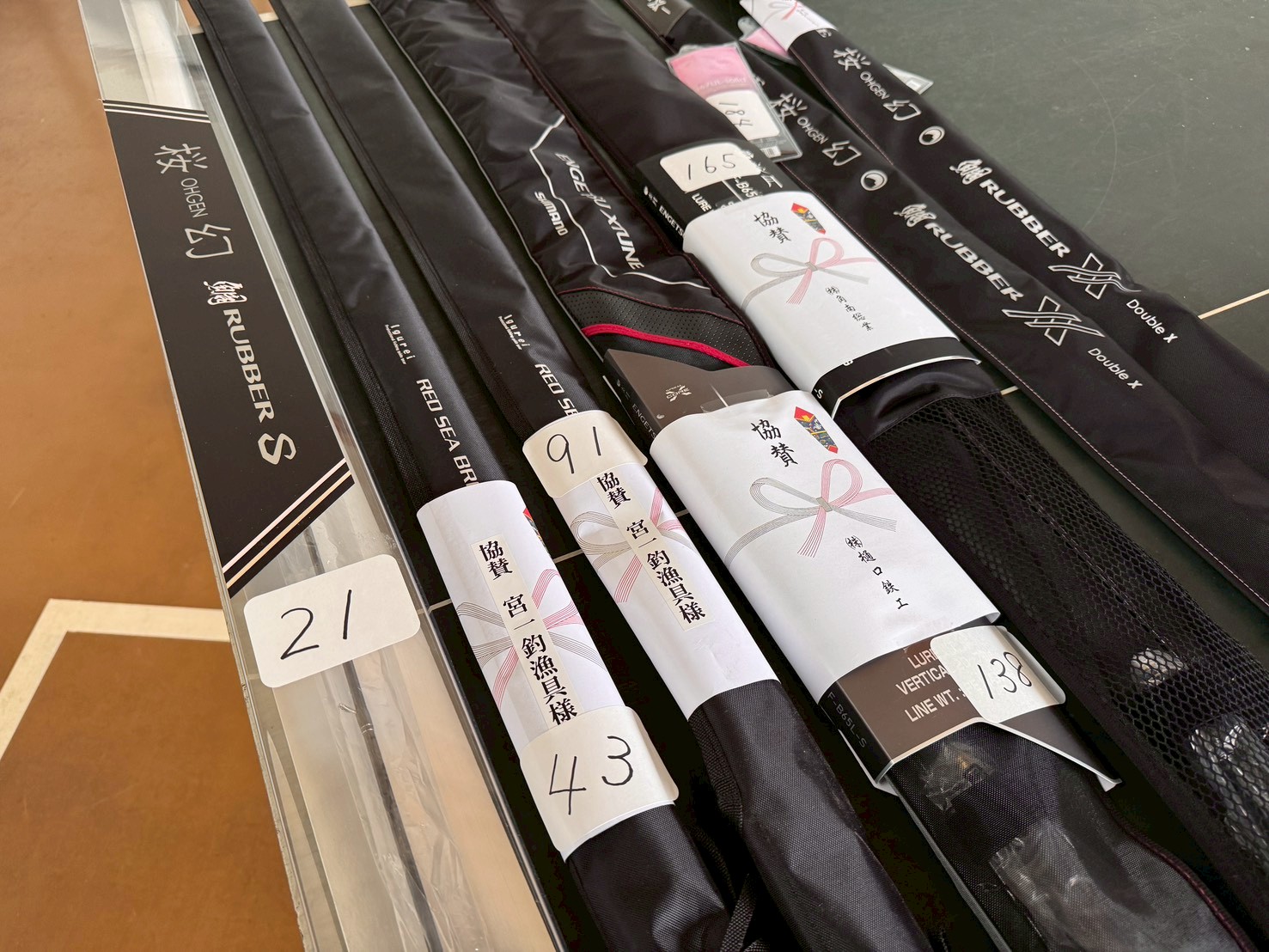 Row of fishing rods in black sleeves with white labels and numbered tags on a display table.